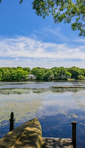 Calm lake in Yarmouth with lily pads, a kayak on the dock, and tree-lined shores under a blue sky