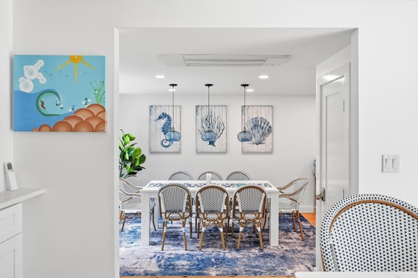 Bright living room with coffered ceiling, large windows overlooking green landscape, blue and white nautical decor, wooden floors, and white furniture.